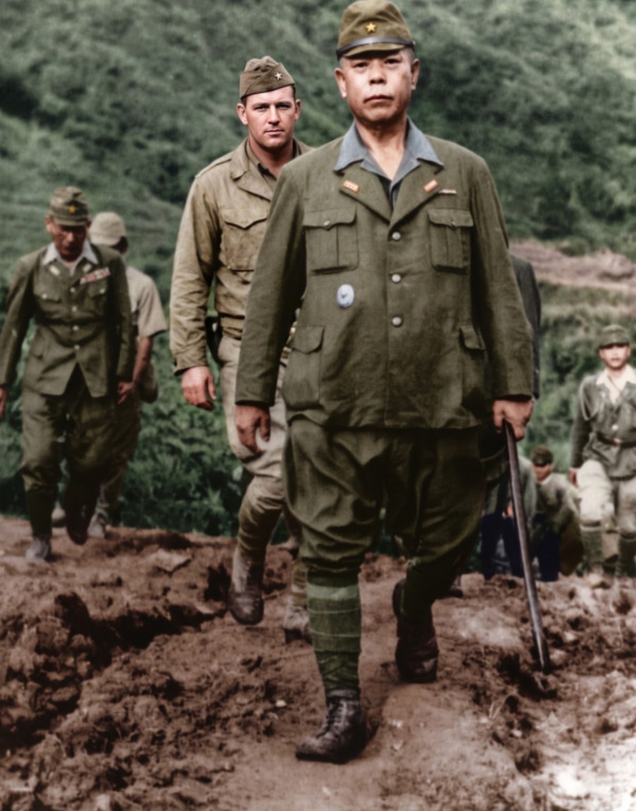 General Yamashita walking down a muddy mountain trail under American escort on the day of his surrender.